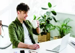 Empreendedor digital, homem sentado com caneca na mão olhando para a tela do notebook em cima da mesa